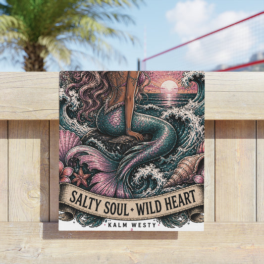Mermaid beach towel with vintage sunset, ocean waves, and "Salty Soul Wild Heart" text on wooden fence, outdoors.