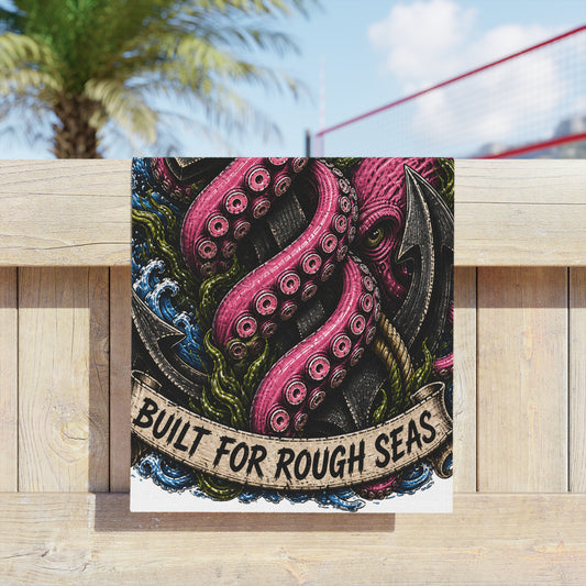 Nautical beach towel with kraken tentacles and anchor design, hanging on a timber fence under a palm tree.