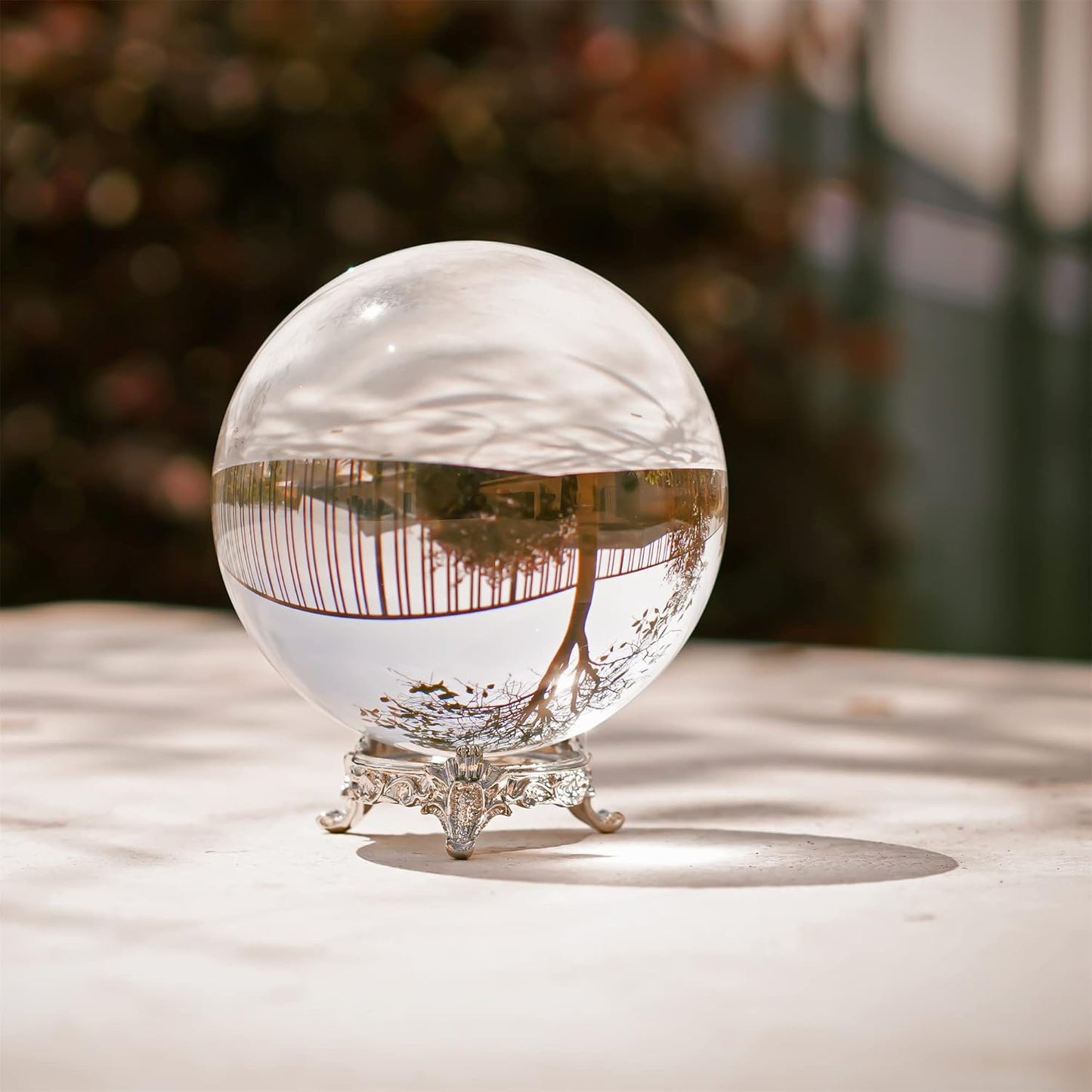 80mm clear K9 crystal ball on silver ornate stand, reflecting an outdoor landscape for photography and divination.