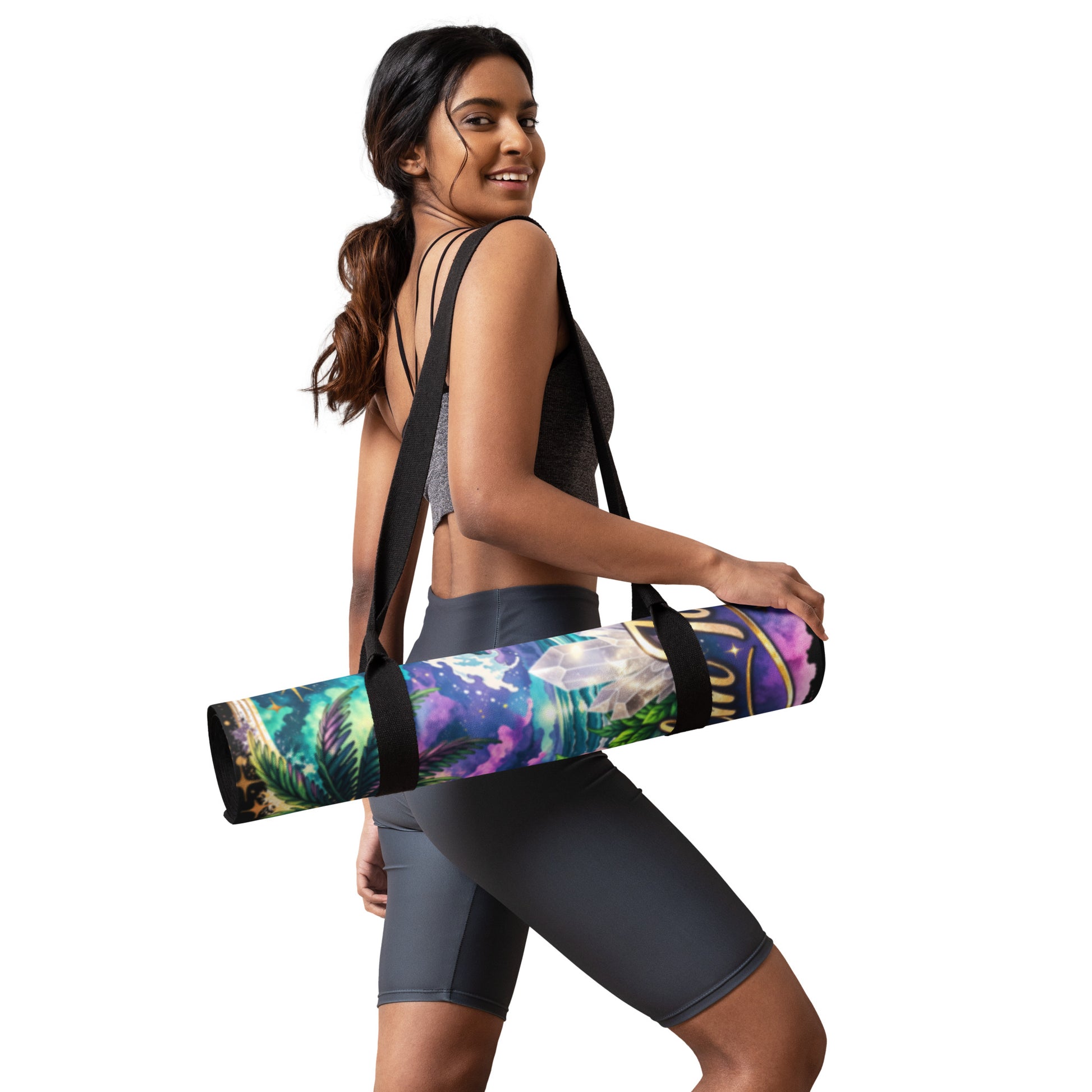 Woman carrying a rolled non-slip microsuede yoga mat with a tropical celestial design using a black shoulder strap.